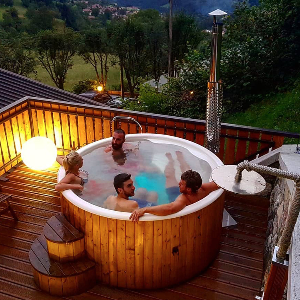 A group of people enjoying the warmth of the KeiCo Deluxe Wood-fired Eco Hot Tub, emphasizing its capacity to comfortably accommodate 4-6 people.