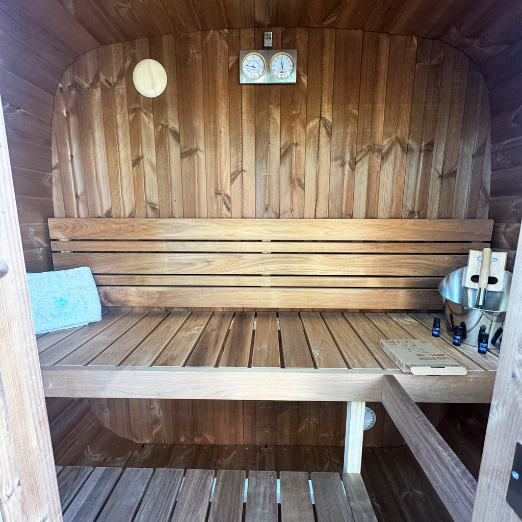 Wooden sauna interior with a bench, towels, and bottles.