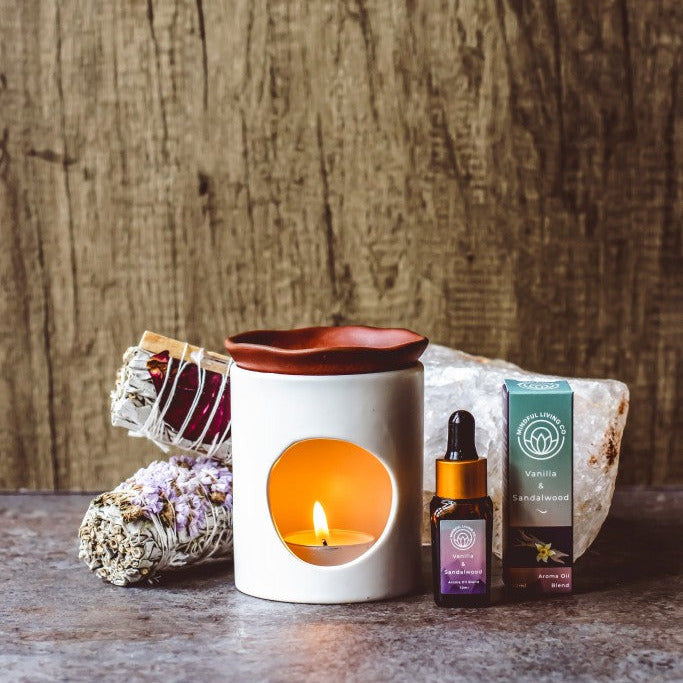 Vanilla & Sandalwood fragrance oil bottle beside creamy vanilla pods and carved sandalwood, lit by a warm burner glow – cosy, grounding, and softly spiced.