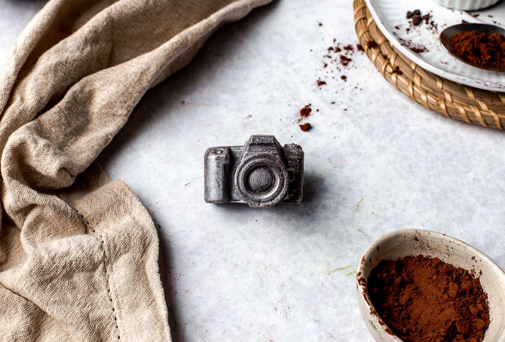 Playful photographer’s chocolate gift set displayed with lens and gear props