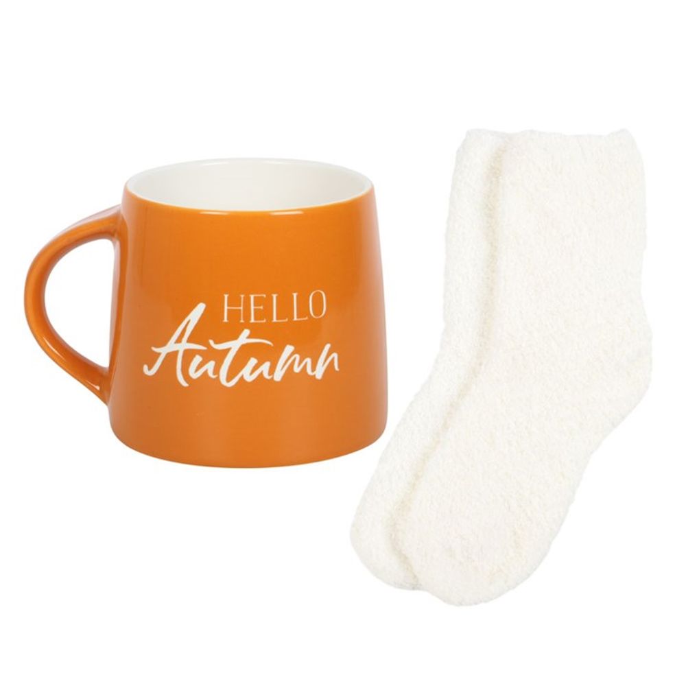 KeiCo's Hello Autumn Mug, brimming with a warm drink, next to plush socks, ready for an autumnal snuggle.