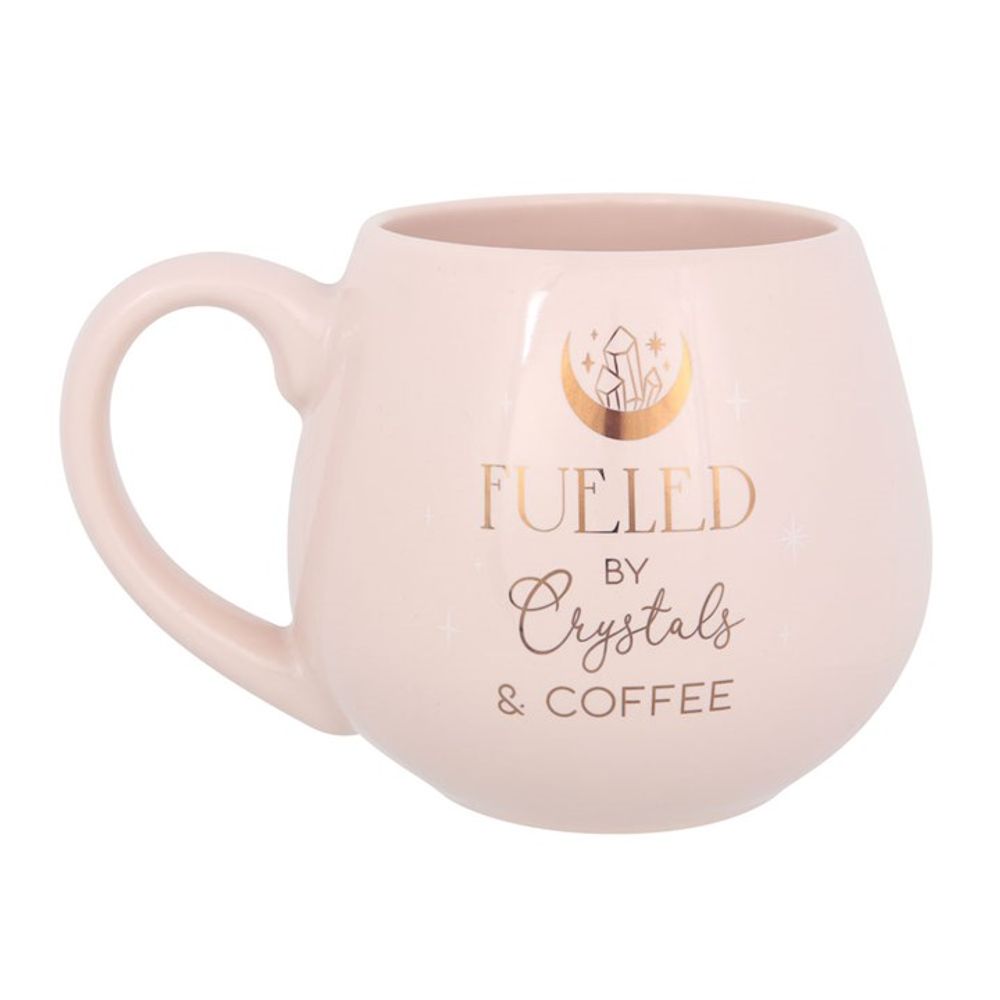 Elegant pink mug with 'Fueled by crystals and coffee' in gold, highlighted by crescent moon design.